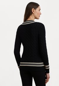 Black knitted sweater with a cable pattern, featuring a striped collar and hem in white and black. Fitted design, ribbed cuffs and bottom.