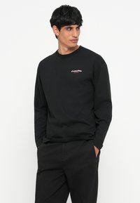 Schwarzer Langarm-Sweatshirt aus Baumwolle, mit Rundhalsausschnitt und pinkem Logo-Stick auf der linken Brust. Einfaches Design und schmaler Schnitt.