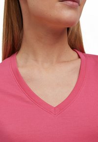 V-hals top in helder roze, gemaakt van soepel katoen. Heeft een comfortabele pasvorm met stikseldetails langs de halslijn.