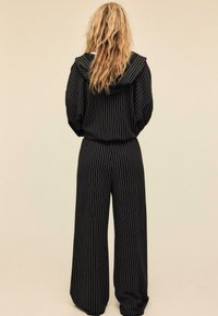 Mustaraidallinen oloasusetti, jossa hupparimallinen yläosa leveillä hihoilla ja väljäntuntuiset housut rentouttavalla siluetilla.