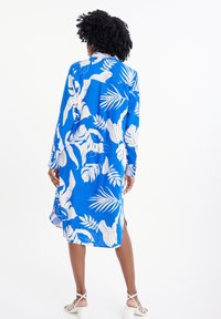Abito blu a maniche lunghe con motivo di foglie tropicali bianche, realizzato in tessuto leggero, con una vestibilità comoda e spacchi laterali.