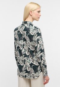 Long-sleeve shirt featuring a dark green background with white swirling patterns. Made of smooth fabric with a classic collar and button closures.
