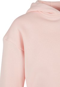 Rózsaszín, puha textúrájú kapucnis pulóver, laza fazonnal. A váll és a nyak környékén varrási részletek láthatóak.