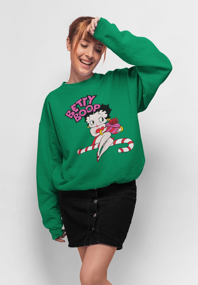 Sweatshirt oversize vert avec un graphisme de dessin animé de Betty Boop, arborant des couleurs vives et un texte audacieux au-dessus du personnage. Jupe en denim noir.