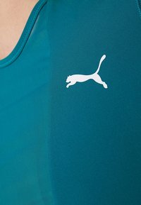 Teal träningslinne med en mjuk textur och en vit Puma-logotyp på vänster sida. Designat för komfort och rörlighet.