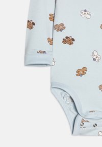 Svetlo modra bodi z dolgimi rokavi s potiskom medvedkov v rjavi in beli barvi. Ima gumbe na dnu in elastične odprtine za noge.