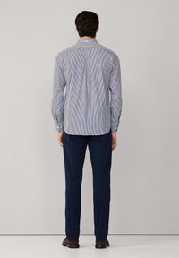 Blauw-witte gestreepte overhemd met knopen, lange mouwen, rugpasdetail, gedragen met marineblauwe broek en bruine schoenen. Glad stoffen textuur.