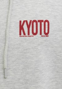 Rød "KYOTO"-tekst med mindre tekst "Kiyomizu-dera Sanjunoto" og japanske tegn på lys grått stoff med hvit snor.