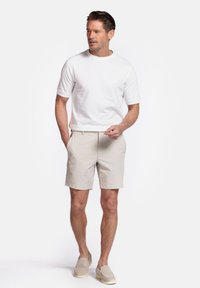 Witte t-shirt met korte mouwen en beige shorts. De shorts hebben een getailleerde pasvorm en een gladde textuur. Lichtgekleurde instap schoenen.