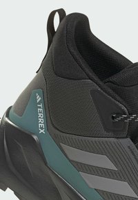 Czarny but sportowy z teksturowaną cholewką, akcentami w odcieniu teal oraz szarymi paskami. Zaprojektowany z wyściełanym kołnierzem dla wsparcia.