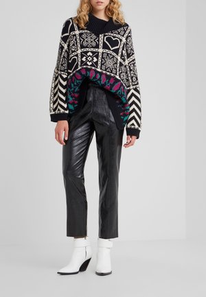 Woman wearing a black and white patterned sweater with colorful accents, black shiny pants, and white ankle boots with block heels.