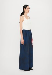 Pantaloni a gamba larga color navy con un sottile motivo tie-dye rosa, dotati di vita alta, pieghe e una texture di tessuto liscia. Accoppiati con un top bianco senza maniche.