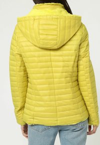 Chaqueta acolchada amarilla con capucha, con un diseño acolchado vertical y un forro suave y peludo alrededor del cuello. Vista trasera con mangas largas.