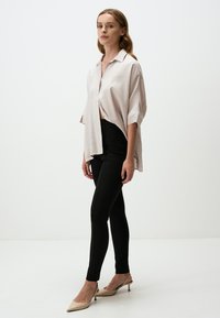 Camicia oversize rosa chiaro con maniche corte, chiusura a bottoni, abbinata a pantaloni neri aderenti e décolleté beige con punta.