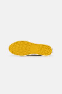 Semelle de sneaker présentant une semelle en caoutchouc jaune texturé avec des motifs en zigzag et des détails circulaires, bordée d'un contour blanc.