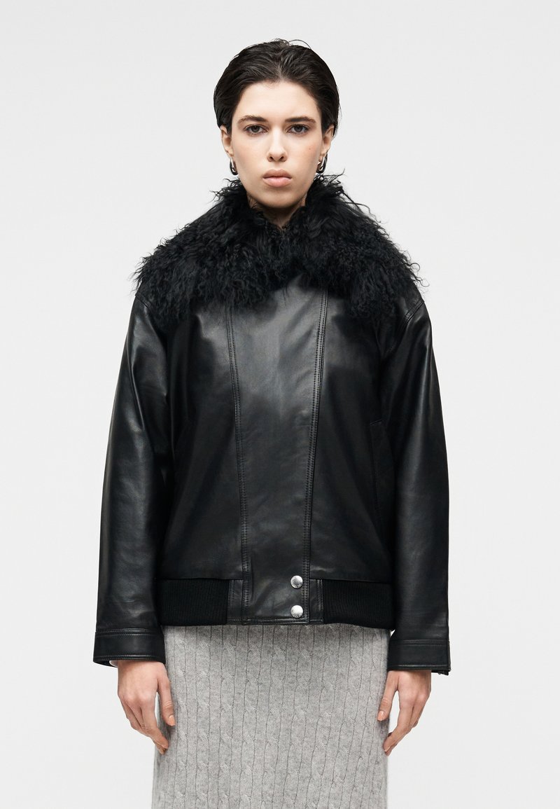 Μαύρο δερμάτινο μπουφάν με χνουδωτό μαύρο γιακά, με εφαρμοστή σιλουέτα, δύο ασημένια κουμπιά και ριμπ μανσέτες. Φορεμένο πάνω από γκρι πλεκτή φούστα.