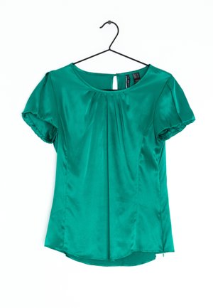 Zielona satynowa bluzka z krótkim rękawem, okrągłym dekoltem, przednimi fałdami i zapięciem na guzik z otworem, wisząca na czarnym wieszaku na białym tle.