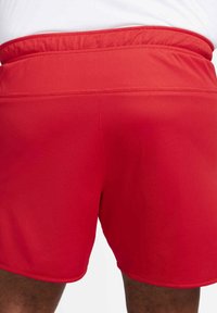 Primo piano di una persona che indossa pantaloni sportivi rossi brillanti e una maglietta bianca, con un focus sulla parte bassa della schiena e le cosce superiori.