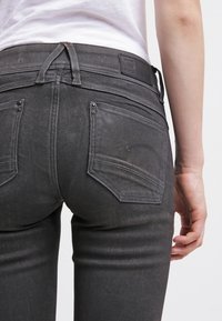 Schwarze Denim-Jeans mit einem schmalen Schnitt, die sichtbare Nähte, fünf Taschen und ein Leder-Logo-Patch am Bund aufweisen.