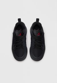 Zapatillas negras hechas de malla y gamuza, con un diseño de corte bajo, cordones negros, acentos de logo rojos y una suela de goma.