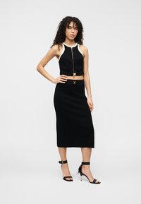 Μαύρο σετ δύο τεμαχίων με αμάνικο τοπ με φερμουάρ και εκρού λεπτομέρειες, συνδυασμένο με εφαρμοστή φούστα μέχρι το γόνατο. Μαύρα ψηλοτάκουνα με λουράκια.