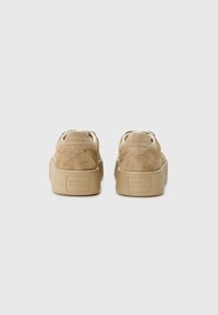 Baskets en suede tan avec une épaisse semelle en caoutchouc. L'arrière présente un logo et un détail de couture, avec des lacets beiges et un col rembourré pour le confort.