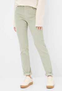Lysgrønne corduroypants med slim fit, der har frontlommer, lynlås og opsmøgte nederkanter, parret med hvide sneakers med en tan sål.