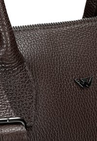 Bruin leren handtas met een gepolijste structuur, voorzien van een ritsluiting en een klein metalen logo accent.