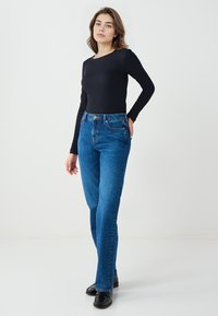 Zwarte lange mouwen top gecombineerd met hoog waargemaakte, lichtblauwe rechte broek. De outfit heeft een klassieke denim structuur en voorzakken.