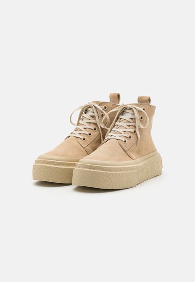 Beige suede high-top sneakers with a thick textured cream sole, round toe, and beige laces, featuring a pull tab at the back.