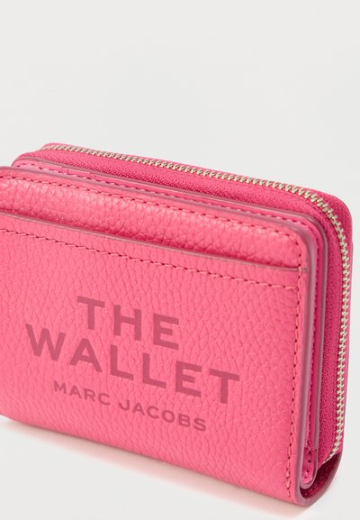 Portefeuille en cuir texturé rose vif avec une fermeture éclair, étiqueté "THE WALLET MARC JACOBS" sur le devant.