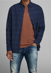 Marinrandig skjorta med knappar över en brun rundhalsad t-shirt, matchad med slitna ljusblå jeans, vilket visar på varierade texturer och färger.