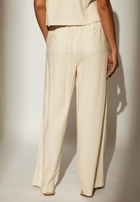 Pantalons beige à jambes larges en tissu texturé. Équipés de deux poches arrière et d'une taille élastique pour plus de confort.