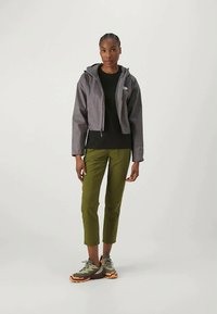 Chaqueta gris corta con capucha sobre una blusa negra, combinada con pantalones oliva ajustados y zapatillas deportivas verde-naranja.