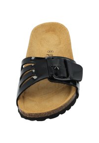 Schwarze Riemensandale mit einem glänzenden Kunststoffriemen, der Ausschnittdesigns und eine Schnalle aufweist, auf einem beigen, samtähnlichen Fußbett und einer strukturierten schwarzen Sohle.