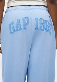 Άτομο που φοράει ανοιχτό μπλε φόρμα με την επιγραφή "GAP 1969" κεντημένη με μεγάλα γράμματα στη πίσω ζώνη της μέσης.