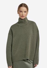 Przesadny sweter z golfem w oliwkowej zieleni. Posiada ściągacze przy rękawach i u dołu, wykonany z fakturowanego, grubego materiału.