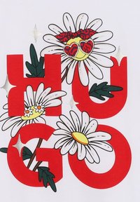 T-shirt blanc avec des lettres rouges en gras "HUGO", accompagnées de graphismes de fleurs marguerites, de feuilles vertes et d'accents argentés et jaunes. Considéré comme un design ludique.