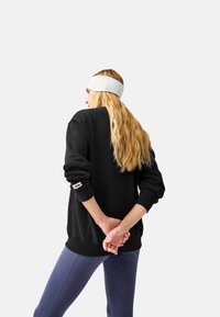Felpa nera con polsini e orlo a coste, caratterizzata da un piccolo logo sul polsino. Abbinata a leggings blu aderenti. Fascia bianca per capelli.