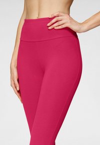 Leggings rosa aderenti realizzati in un tessuto elasticizzato con una vita ampia e liscia e senza cuciture visibili, che evidenziano una silhouette snella.