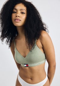Groene katoen bralette met een diepe V-hals en verstelbare bandjes, met een contrastlogo-band met rode, witte en blauwe accenten.