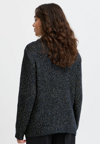 Sweter dzianinowy w ciemnym niebieskim kolorze z jasnymi akcentami w formie drobnych plamek, o luźnym kroju, z długimi rękawami oraz prążkowanymi mankietami i dołem.