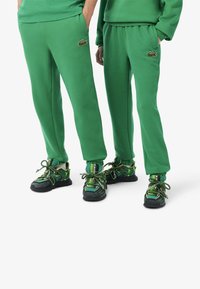 Gröna bomullsträningsbyxor med ribbad mudd, med en liten logotypapplikation. I kombination med gröna och svarta sneakers med texturerade snören.