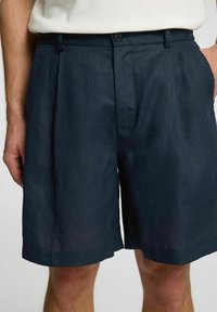Marineblå linnedshorts med plisseret front, knaplukning og sidelommer, med en afslappet pasform og glat tekstur.