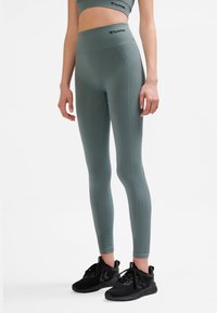 Leggings a vita alta, aderenti, in tessuto verde tenue con texture a coste, caratterizzati da una cucitura blu a contrasto e una vita con logo.