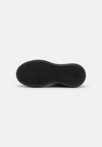 Semelle de chaussure noire mettant en avant un design de bande de roulement ondulé et un motif strié, fabriquée en caoutchouc, avec des bords arrondis pour une meilleure adhérence.