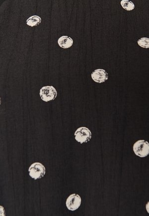 Tissu noir avec des pois blancs irréguliers éparpillés, chaque point montrant des bords texturés et usés ainsi qu'une coloration inégale.