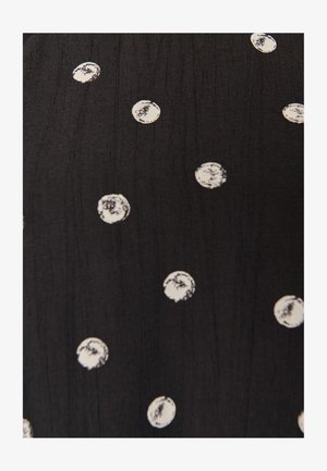 Tissu noir avec des pois blancs irréguliers éparpillés, chaque point montrant des bords texturés et usés ainsi qu'une coloration inégale.