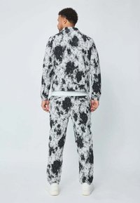 Homme de dos, portant une veste et un pantalon à motif abstrait noir et blanc assortis, avec des baskets blanches.
