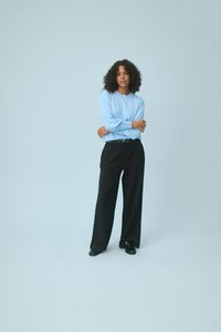 Haut à manches longues bleu clair avec tissu texturé, associé à un pantalon large noir. L'ensemble comprend une ceinture simple et des chaussures plates noires.